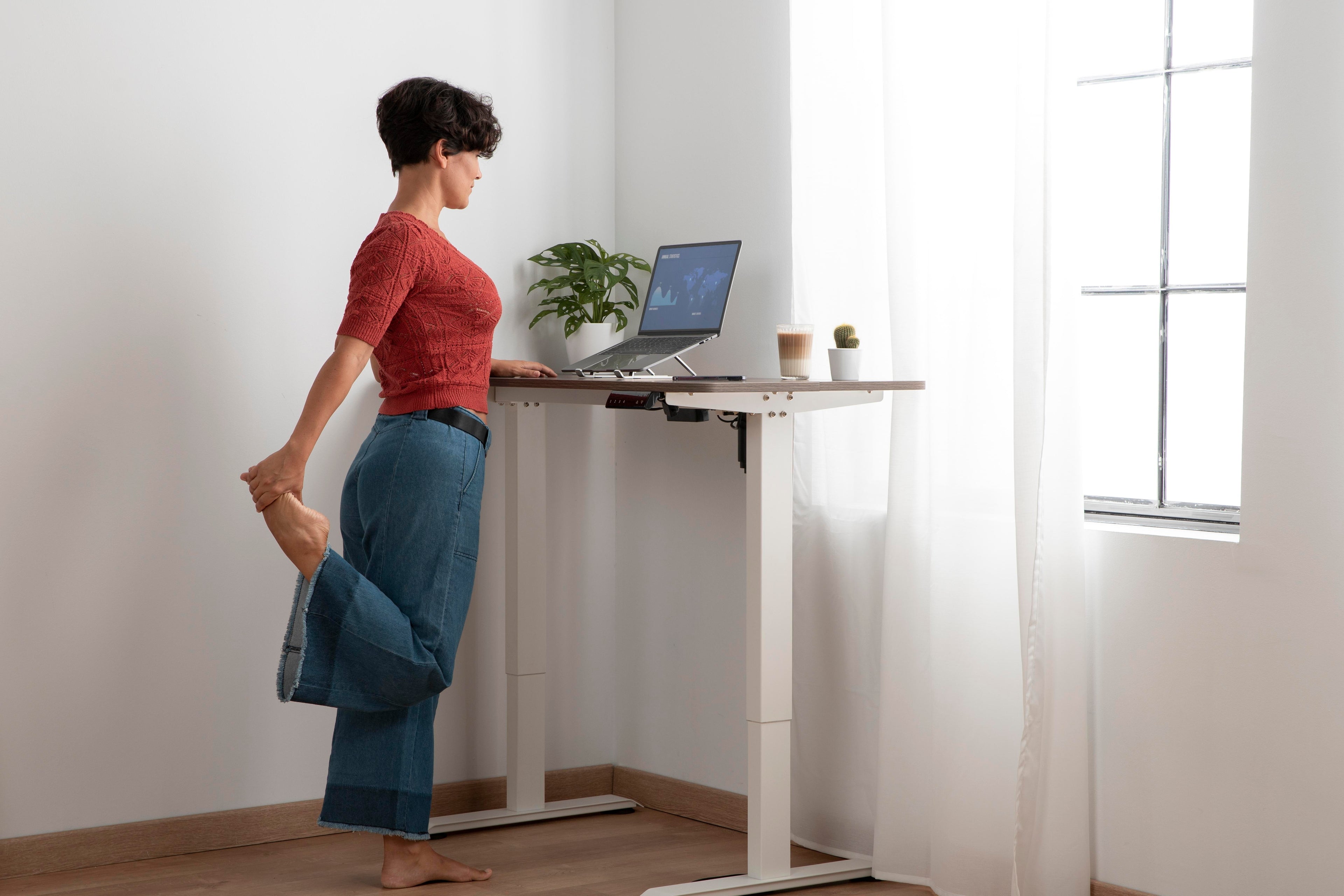 A woman working at a standing desk in a modern home office, adjusting her laptop height with good posture to show the pros and cons of using a standing desk for remote work.