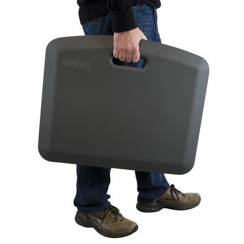 Person carrying a dark gray 18"x22" EcoLast Portable Standing Mat with an integrated handle.