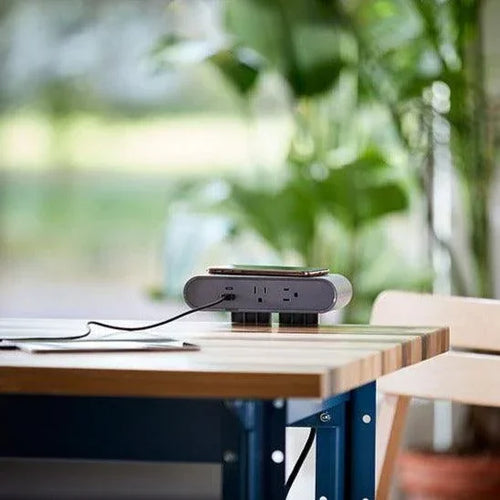 Gray Ellipse Qi wireless edge-mount power block with phone, dual AC outlets, USB-A, and USB-C ports on a wood desk.