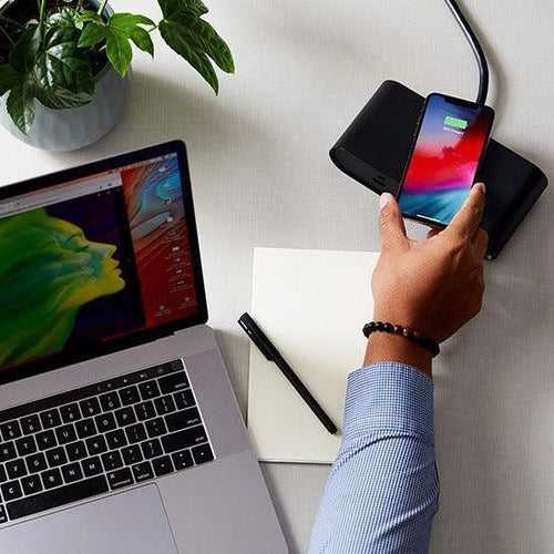 Black Ellipse Qi wireless power block with dual AC, USB-A, and USB-C ports, charging a smartphone on a desk.
